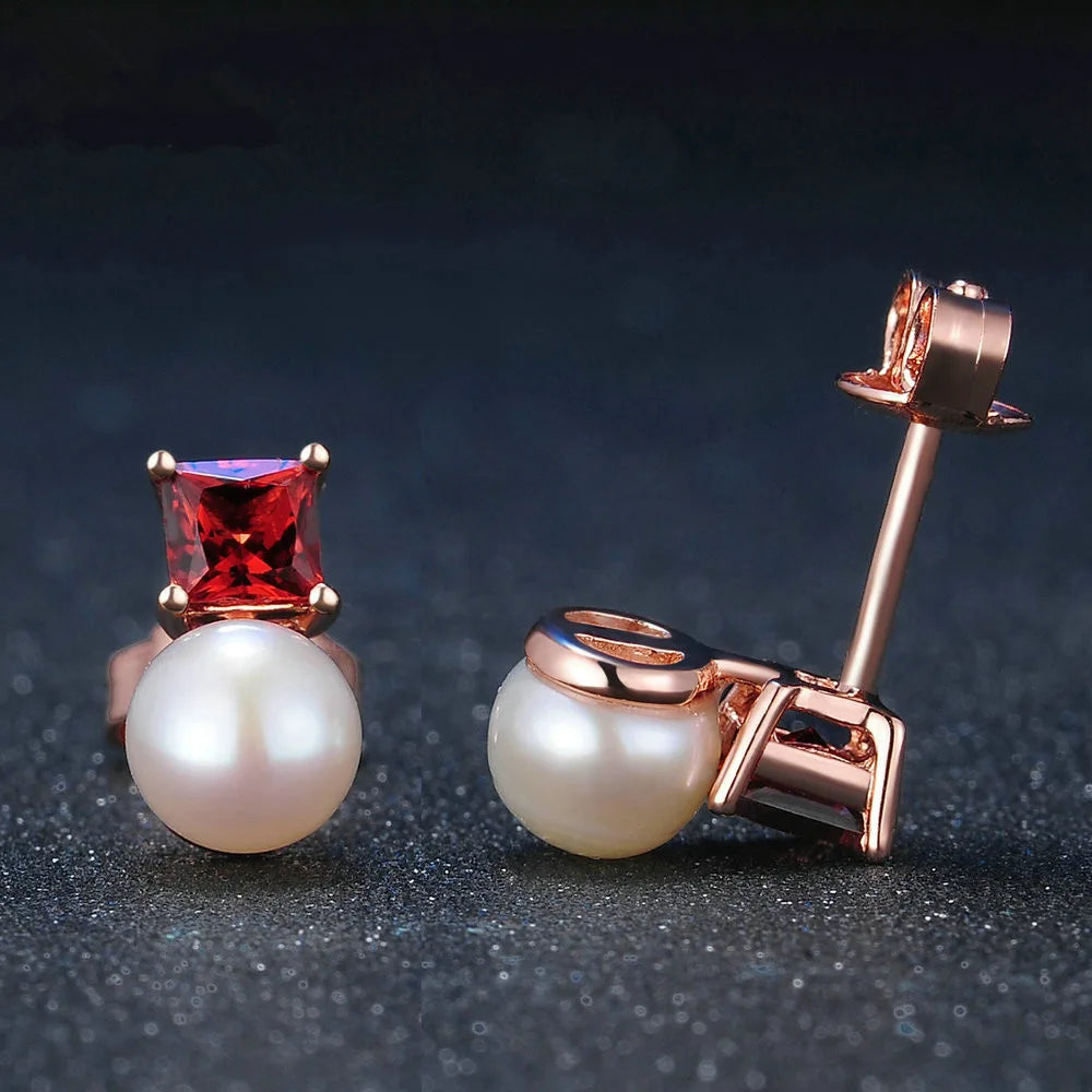 Pair of pearl earrings with rose gold and red gemstone on a dark background