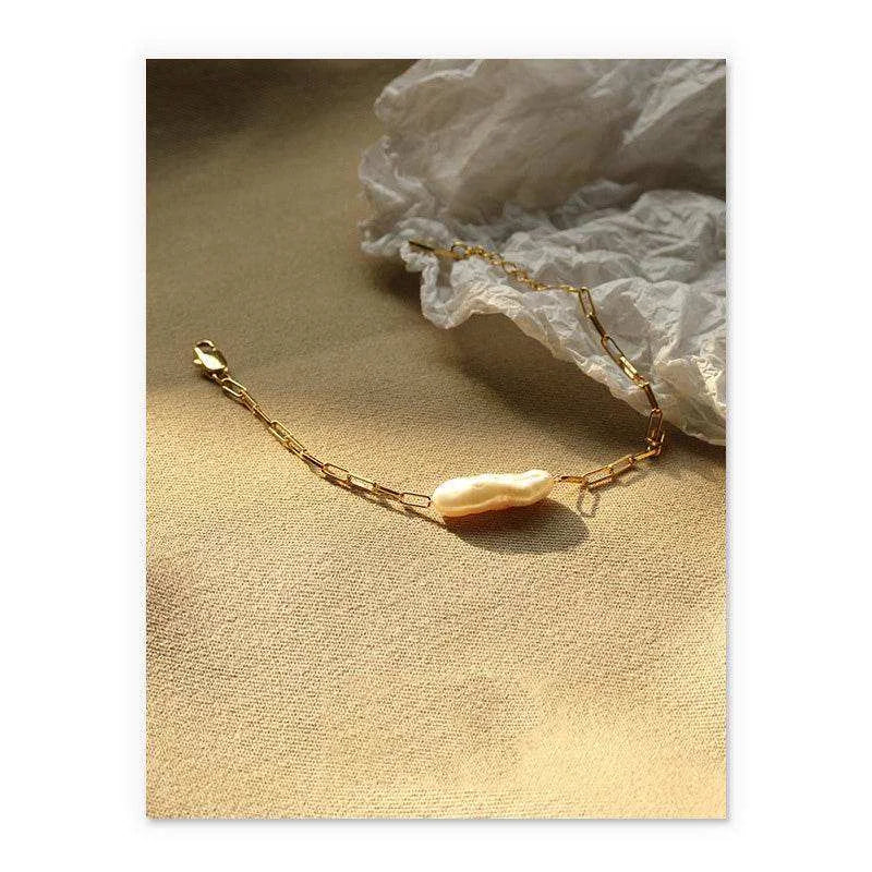 Gold bracelet with a pearl on a textured beige surface