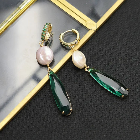 Pair of earrings with pearls and green teardrop stones on a reflective surface.