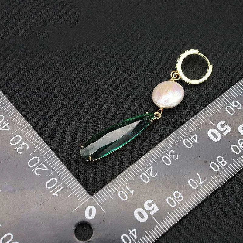 Gold earring with a green teardrop and pearl on a black background with a ruler for scale.