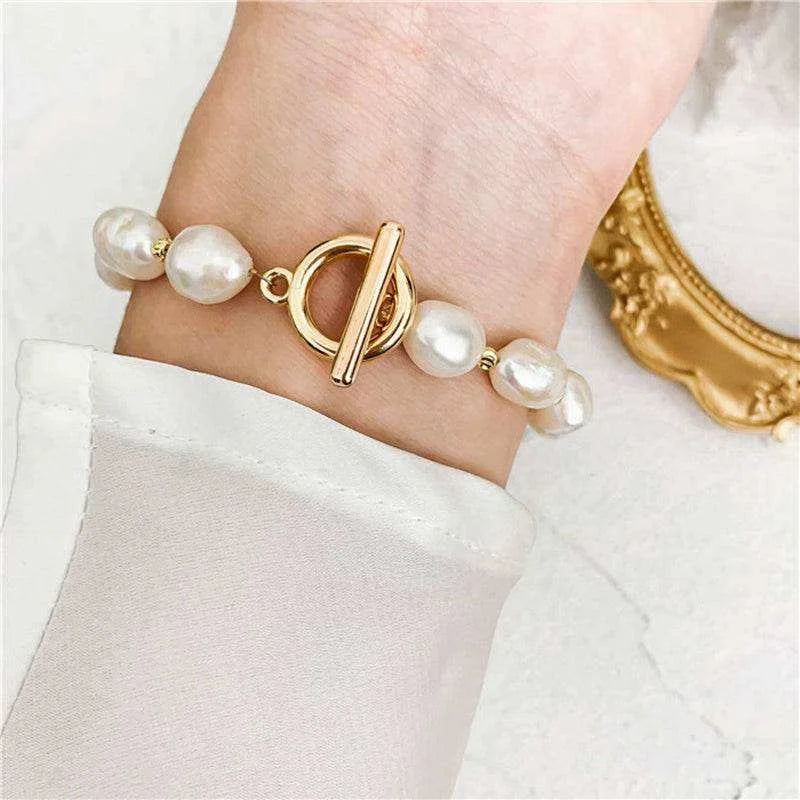 Pearl bracelet with a gold clasp on a wrist, against a white background.