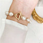 Pearl bracelet with a gold clasp on a wrist, against a white background.