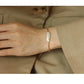 Gold bracelet with a large pearl worn on a wrist against a beige background