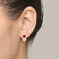 Close-up of an ear wearing a red gemstone and pearl earring against a neutral background
