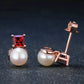 Pair of pearl earrings with rose gold and red gemstone on a dark background
