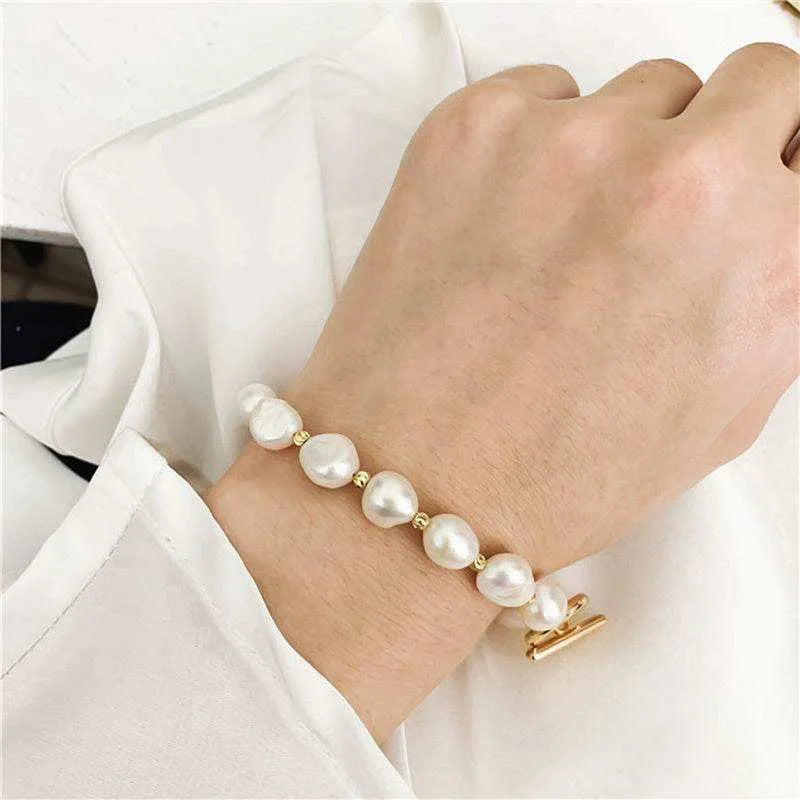 Pearl bracelet with gold clasp on a wrist against a white background