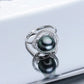 Silver ring with two black pearls on a reflective surface