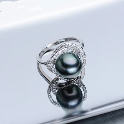 Silver ring with two black pearls on a reflective surface