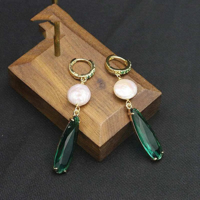Pair of earrings with green teardrop and pearl-like stones on a wooden stand.