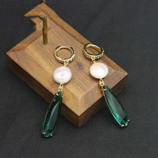 Pair of earrings with green teardrop and pearl-like stones on a wooden stand.
