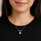 Woman wearing a gold necklace with a pink pearl pendant against a black background