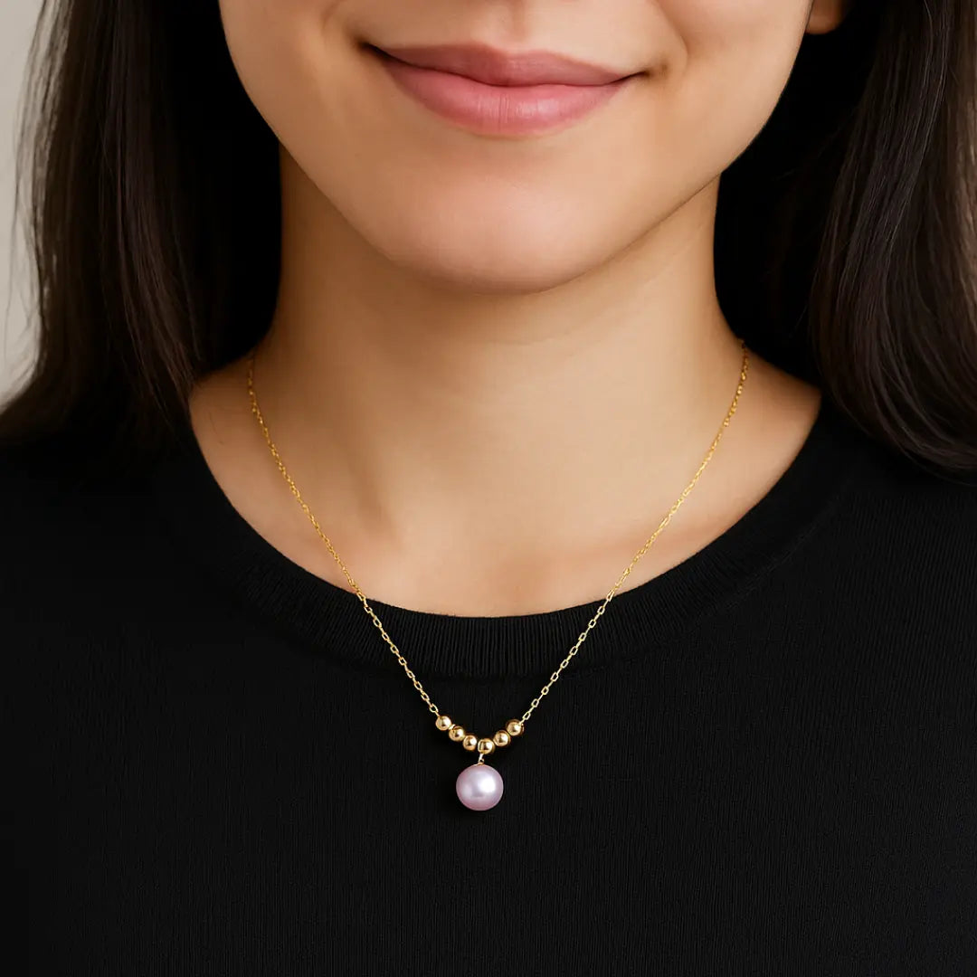 Woman wearing a gold necklace with a pink pearl pendant against a black background