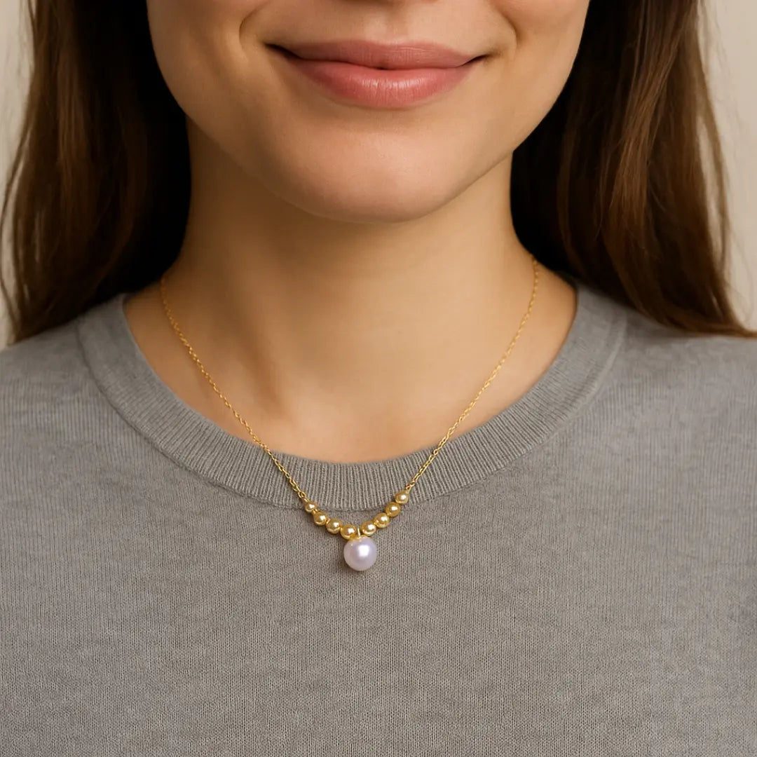 Close-up of a person wearing a gold necklace with a pearl pendant.