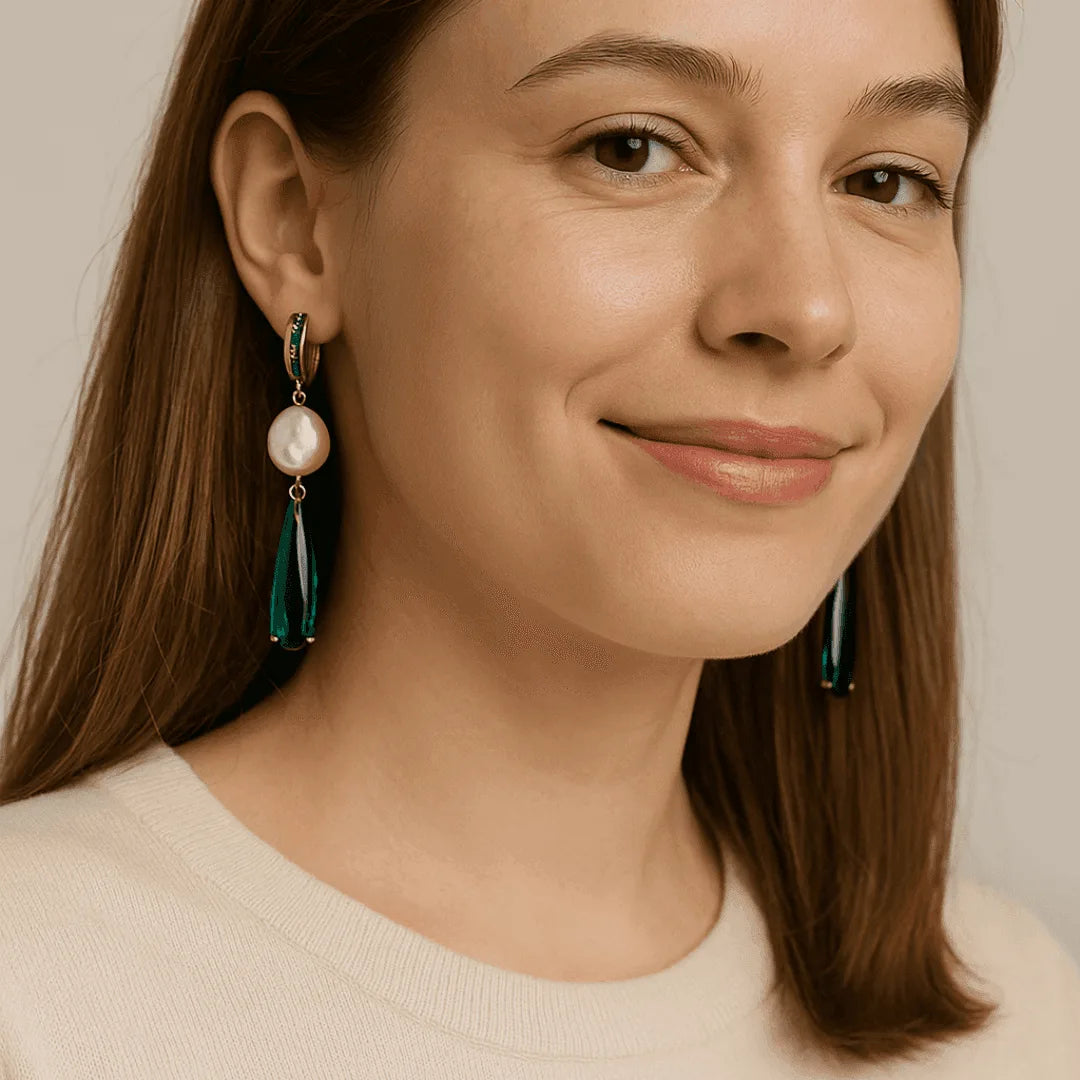 Woman wearing pearl and green teardrop earrings with a neutral background