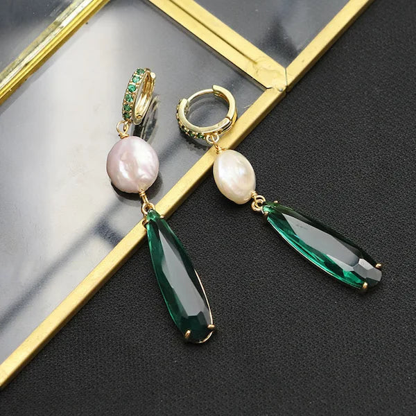 Pair of earrings with pearls and green teardrop stones on a reflective surface.